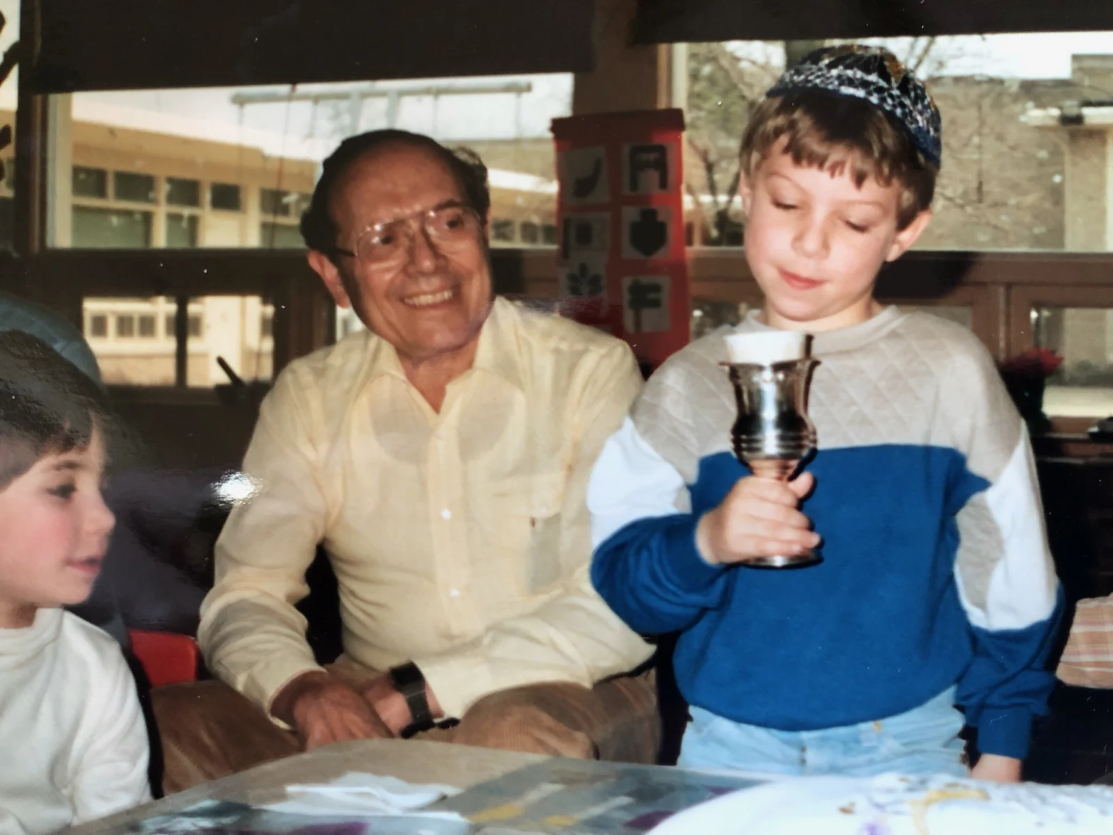 Young Matt Goodman holding a Kiddush cup with his grandfather beside him